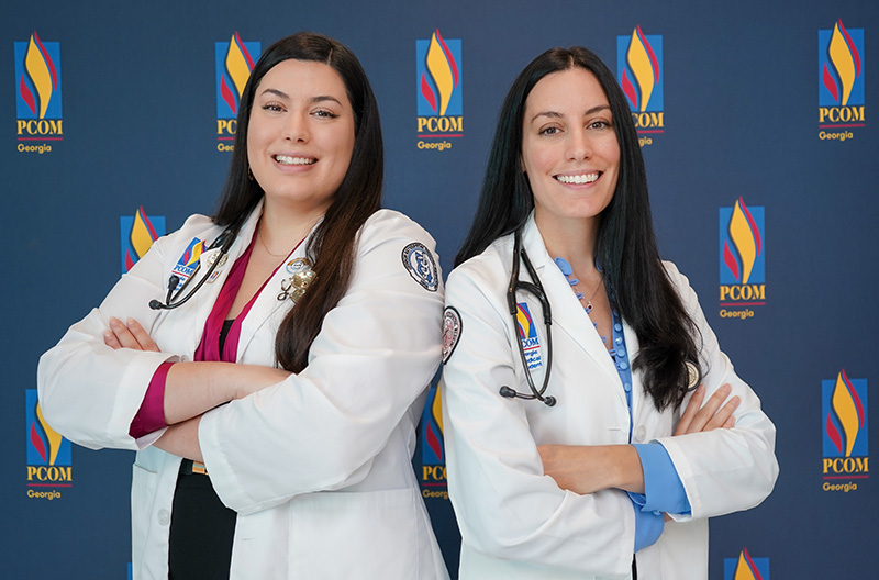 Medical students and sisters Jessica and Danielle Myara pose in their white coats at PCOM Georgia