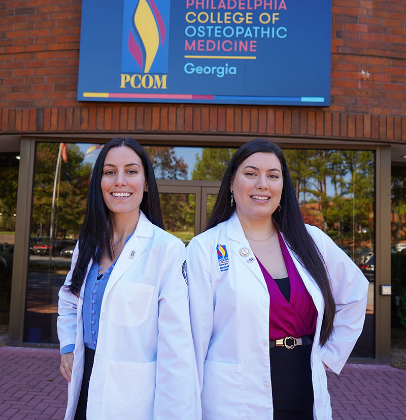 Jessica and Danielle Myara smile in front of PCOM Georgia's front doors