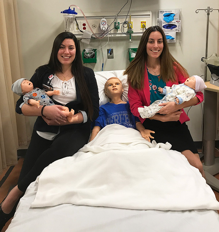 Jessica and Danielle Myara hold pediatric training mannequins in PCOM Georgia's Simulation Center