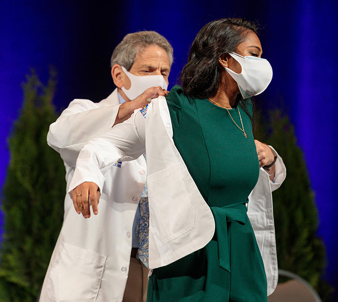 A student doctor and member of the PCOM Georgia DO Class of 2025 receives their white coat from a faculty member