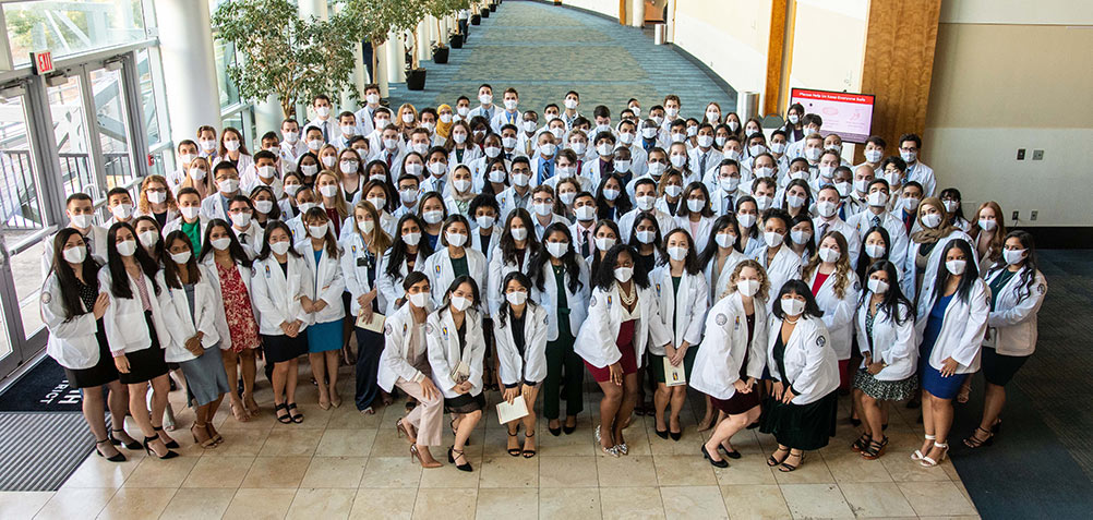 PCOM Georgia's DO Class of 2025 smiles while masked in a group shot for their White Coat Ceremony