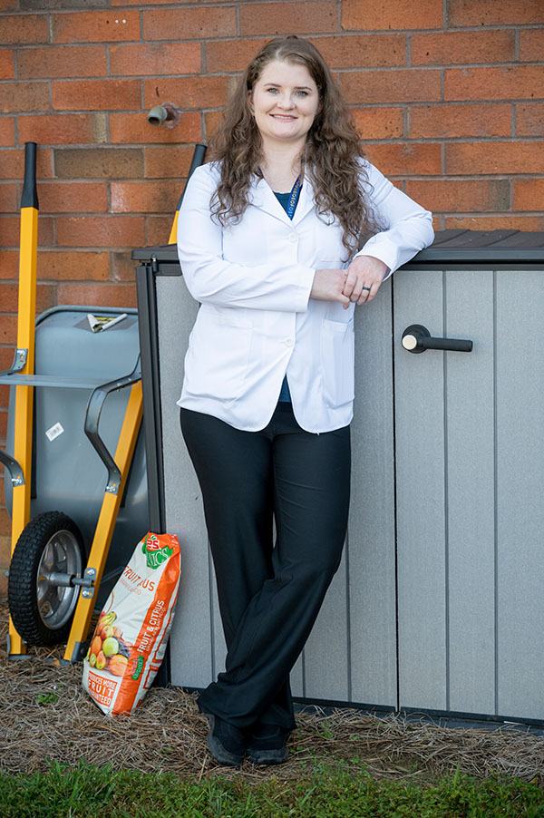 PCOM Georgia med student Jaci Carithers smiles as she leans against a shed during a research project on lead contamination in soil