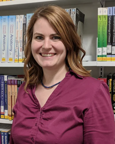 Meghan Di Rito Wegendt, MLIS, stands in front of bookshelf