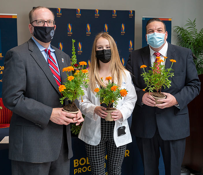 PCOM Georgia medical student Candice Tate holds a marigold flower and stands with the body donor program coordinator and a donor family member.