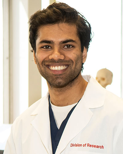 Headshot photograph of Vishwant Tatagari (DO '21) smiling in his white coat in the PCOM Anatomy Lab