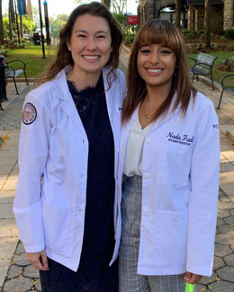Briana Krewson (DO '23) and Nada Fadl (DO '23) wear their student physician white coats and smile on a PCOM pathway.