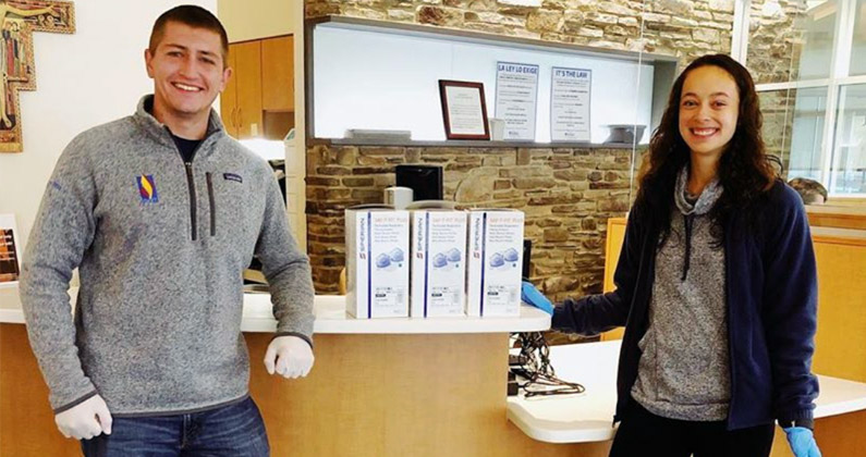 Two PCOM medical students smile as they deliver boxes of new protective face masks to a healthcare center.