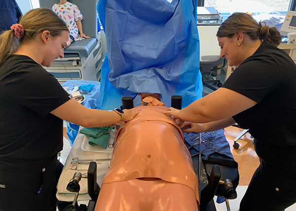 Two medical students prepare for surgery over a simulation mannequin