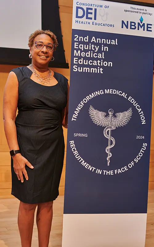 PCOM's Chief Diversity and Community Relations Officer Marcine Pickron-Davis poses with the 2nd Annual Equity in Medical Education Summit banner