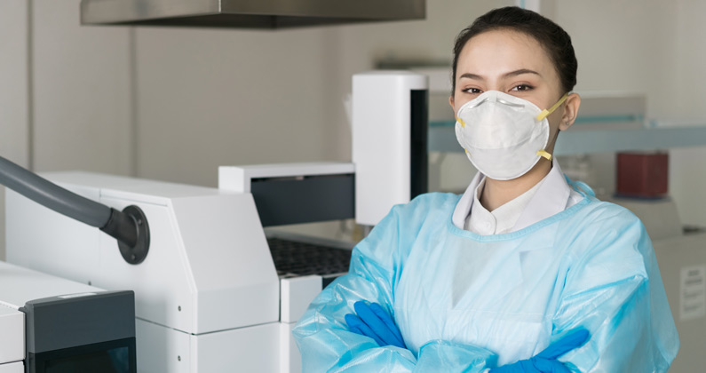 Female grad student wears protective gown, gloves and face mask inside a research laboratory.