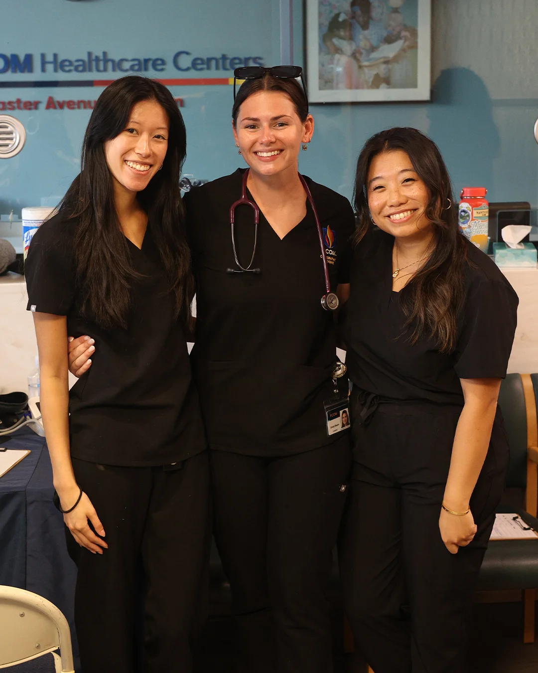 PCOM students in black scrubs pose for a photo with their arms around each other
