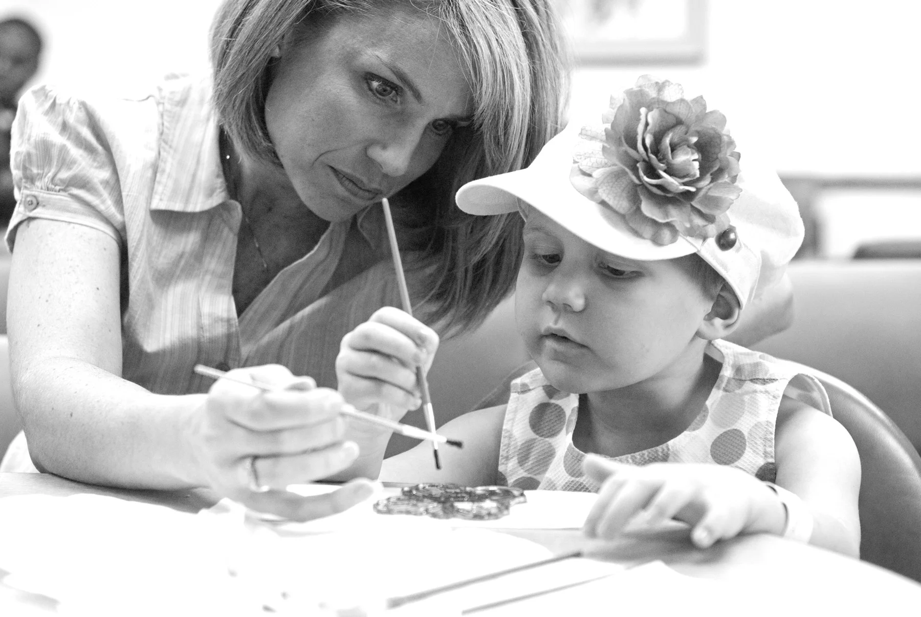 Black and white photo of young cancer patient Ellie Koerner doing arts and crafts with a caretaker at CHOP. FOH/ALSF photo by David Simchock