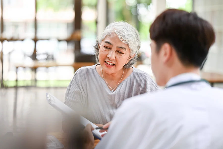Elderly woman and a physician smile as they review info on a clipboard in Memory Center at PCOM