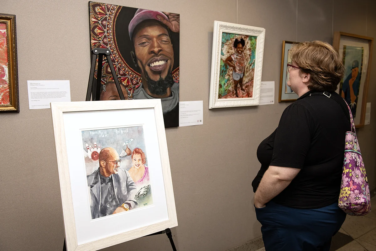 A PCOM staff member views a portrait painting on a wall as part of the Souls Shot Portrait Project: Philadelphia Vol. 8 being hosted at PCOM's campus