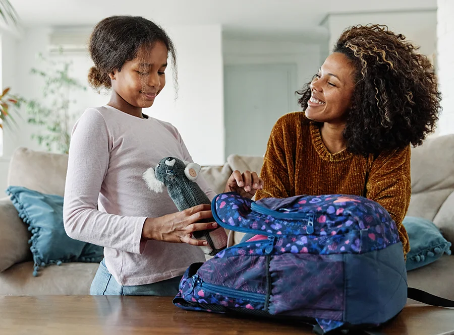 A mother and child work together to pack a backpack with supplies during a back-to-school routine