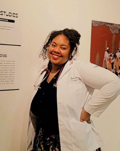 Janita Aidonia Matoke (DO ’26) stands in a white lab coat next to pieces from her museum exhibit