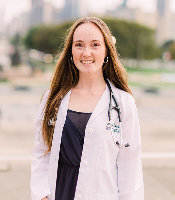PCOM med student and Myo/Nog cell researcher Mara Crispin wearing her white coat in front of the Philly skyline