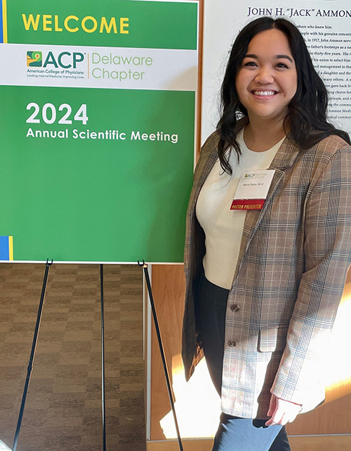 PCOM med student Jillianne Santos smiling beside a sign for the Delaware Abstract Competition by the American College of Physicians (ACP)