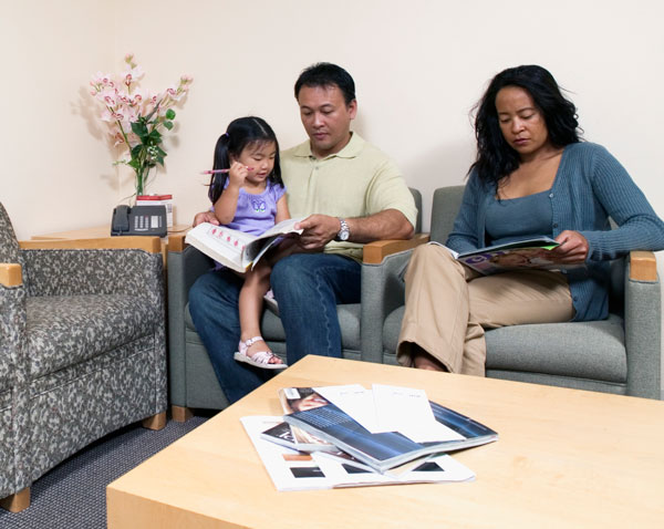 Parent reads book to child while seated in medical office waiting area
