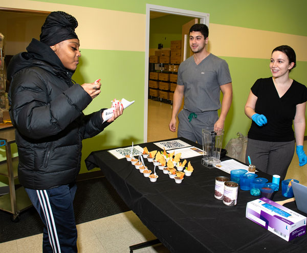 PCOM students look on as healthcare center visitor samples a snack from their food demonstration
