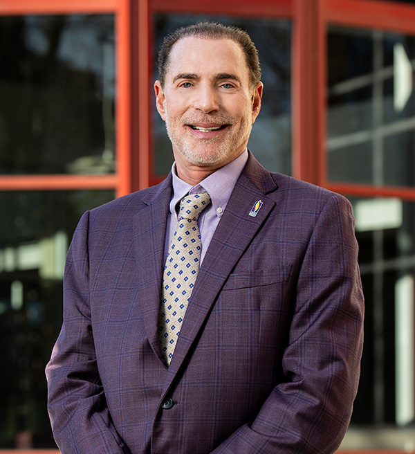 Professional photo of Howard A. Hassman, DO '83 standing in front of the classroom learning building at PCOM