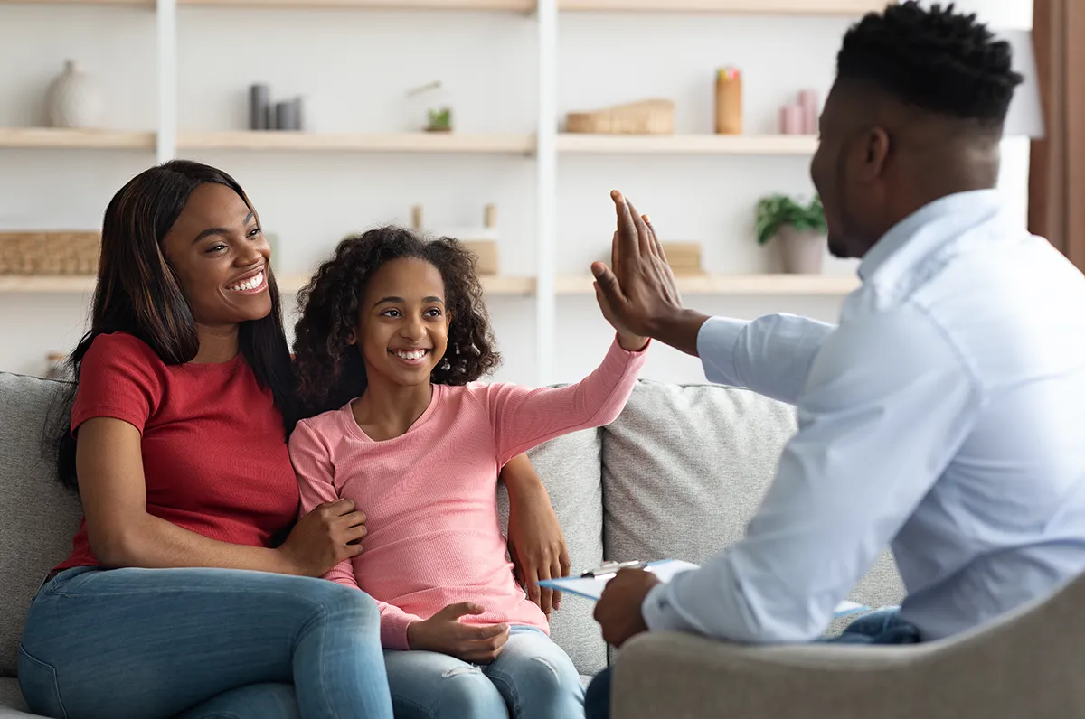 A PCOM psychologist gives a high five to a young patient alongside a parent during a pediatric behavioral service appointment