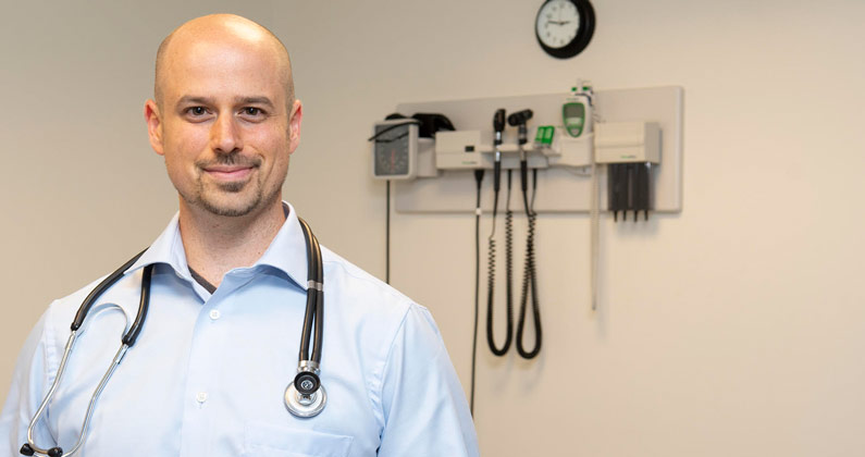 Jason Kaplan, DO ’13, clinical assistant professor, cardiology, smiles in a patient exam room.