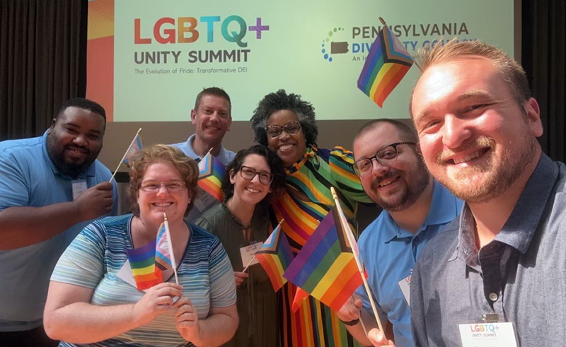 Adrienne Jones and PCOM admissions staff smile and hold rainbow LGBTQIA pride flags at a summit