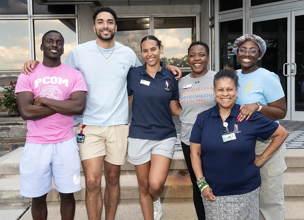 PCOM students and staff, who volunteered to help with the Opportunities Academy program, smile in a group photo in front of one of PCOM's campus buildings