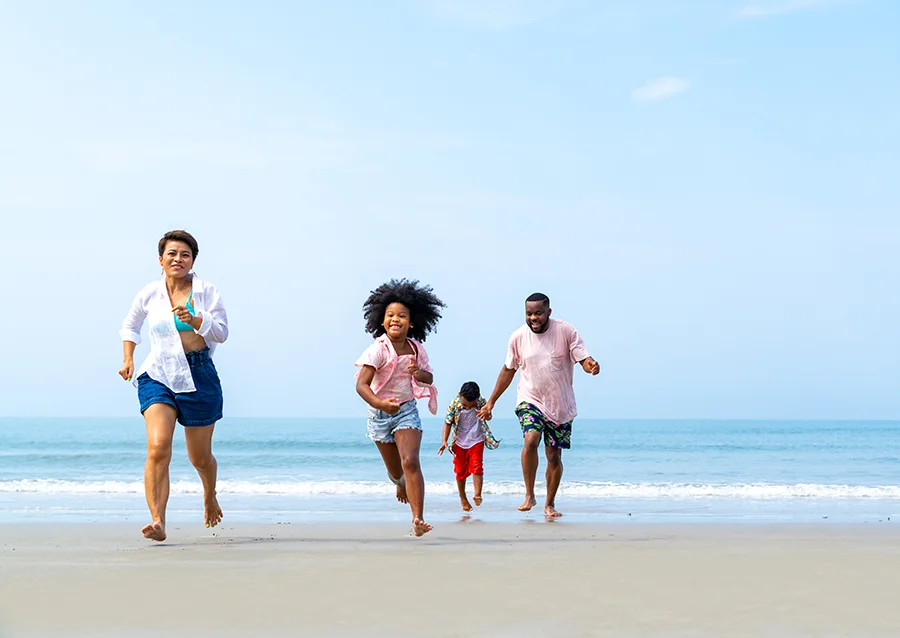 Two Black parents and kids smile and run on a beach during vacation