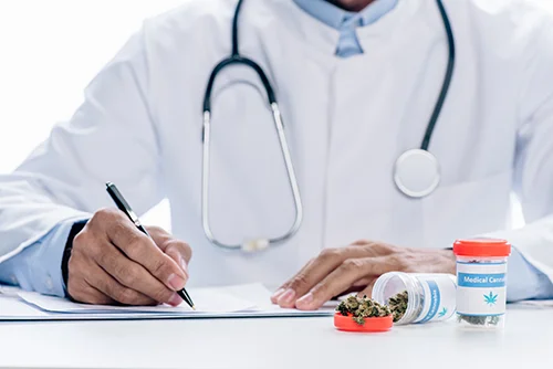 Close up of doctor writing on prescription pad and medicine jar filled with medical grade cannabis