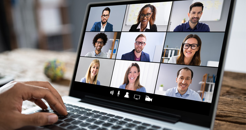 Business woman's hand using a laptop. The screen shows multiple staff and faculty smiling and discussing on a video conference.