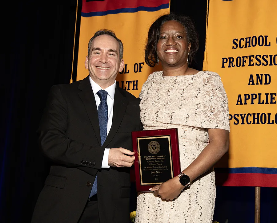 PCOM's Dr. Scott Glassman and positive psychology graduate Lori Niles smile on stage with an award