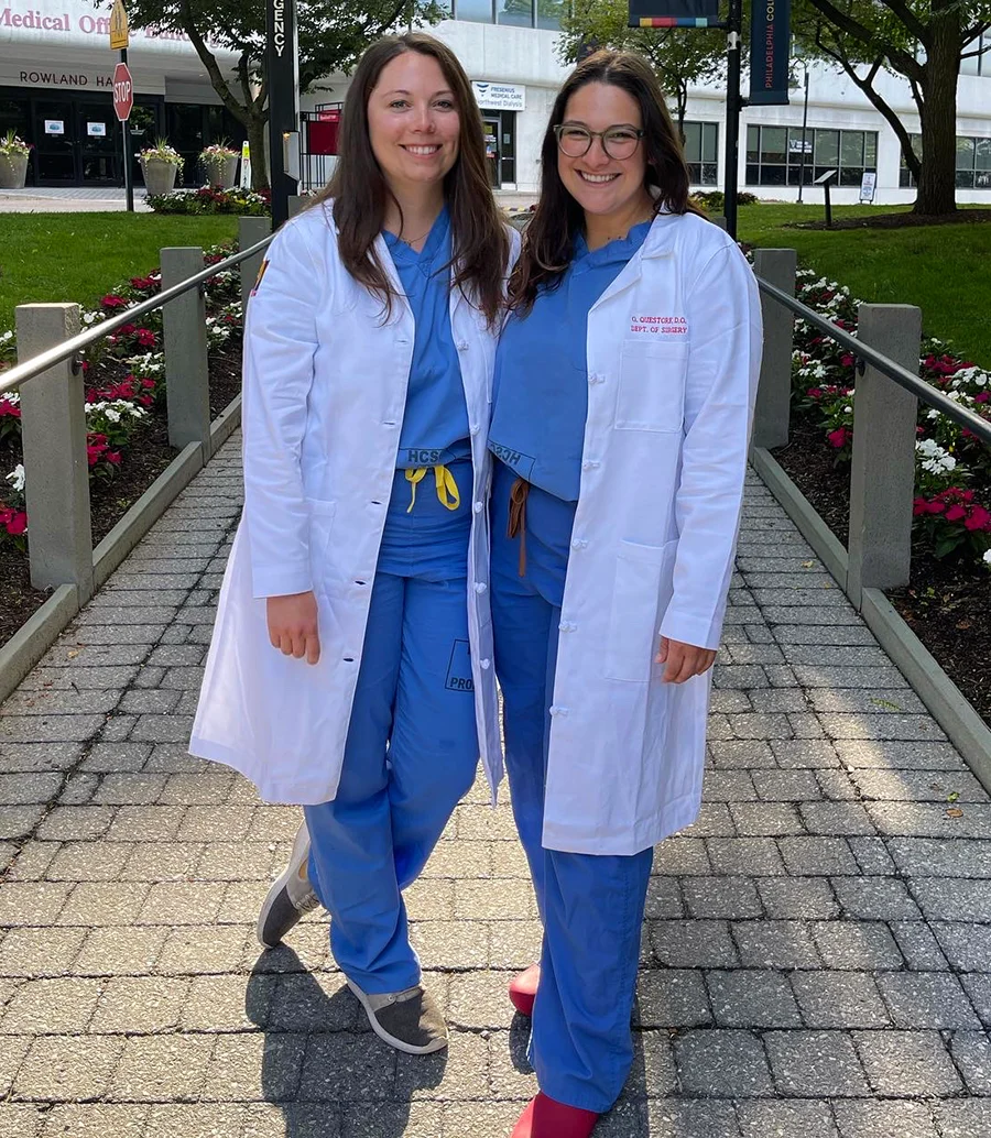 PCOM alum and surgery resident Arielle Worth, DO, smiling with a friend in her physician white coat on PCOM's campus
