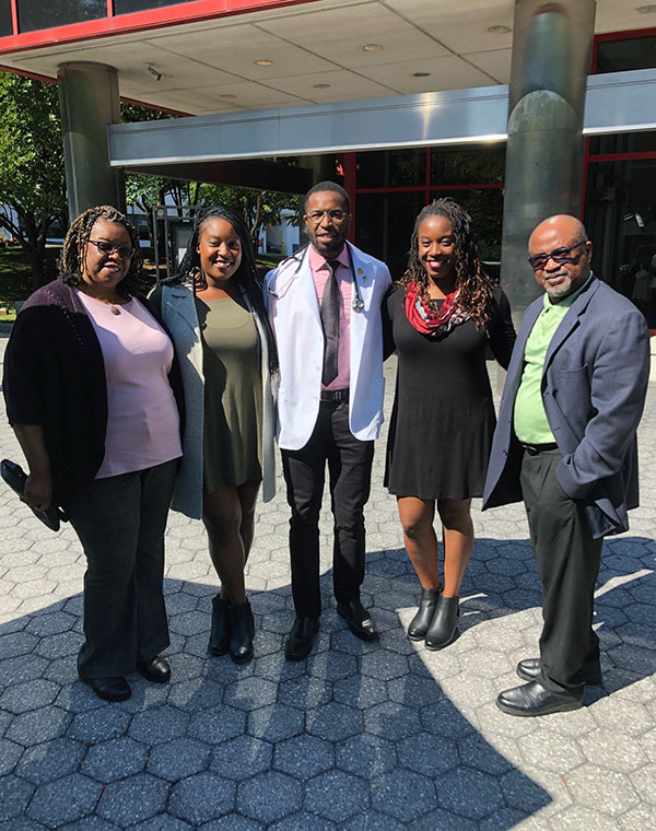Frederick Okoye (DO '24) smiling in a group photo with his family outside of PCOM's campus buildings