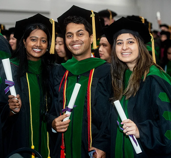 PCOM students in commencement regalia smile while holding diplomas