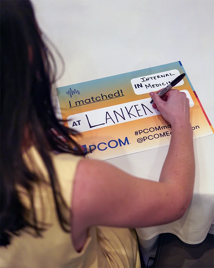Overheard shot of a PCOM medical student writing out where she matched on a celebratory sign during the College's annual Match Day event