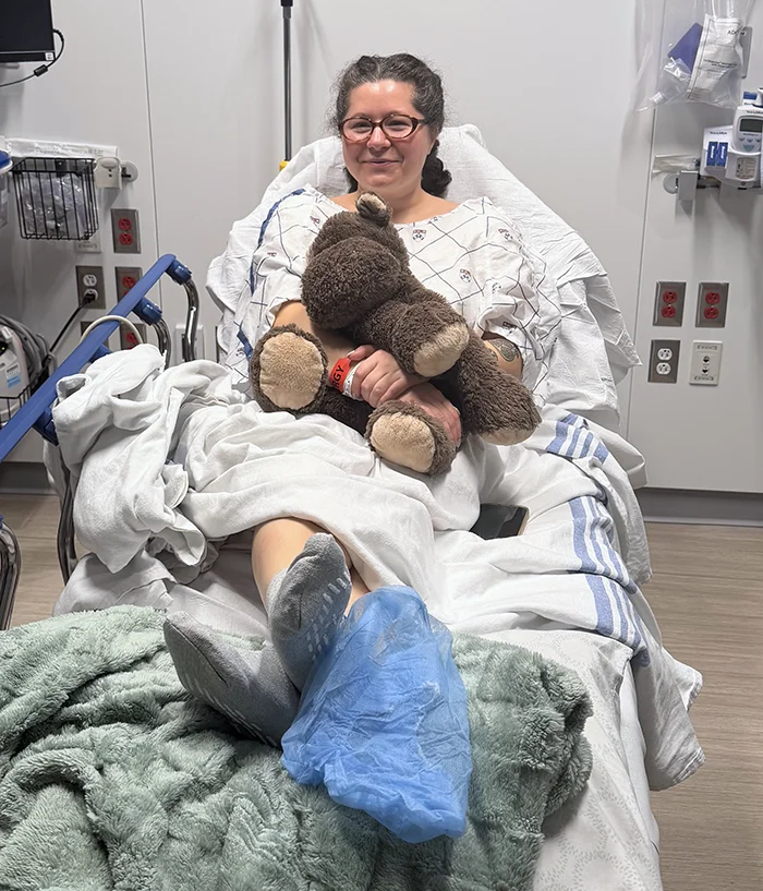 Hannah Callahan smiles in a hospital bed while holding a teddy bear after a kidney donation procedure