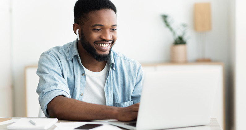 PCOM medical student wearing ear buds and using a laptop on a desk at home to access online learning.