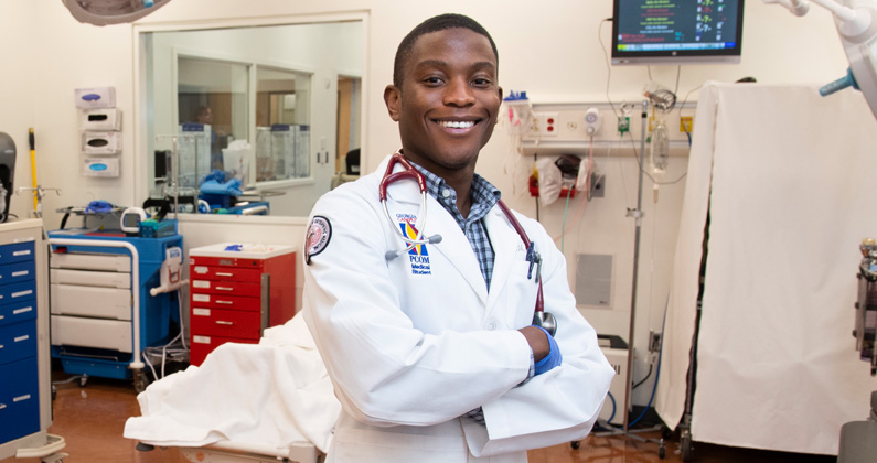PCOM Georgia medical student smiling and standing in the surgery simulation center wearing a student physician white coat.
