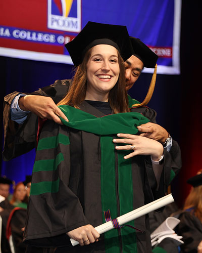 PCOM student stands on stage at commencement ceremony