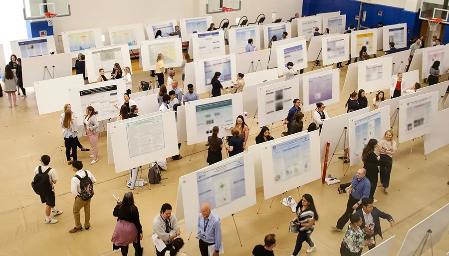Aerial photo of PCOM's Student Activities center gymnasium filled with rows of research posters and attendees.
