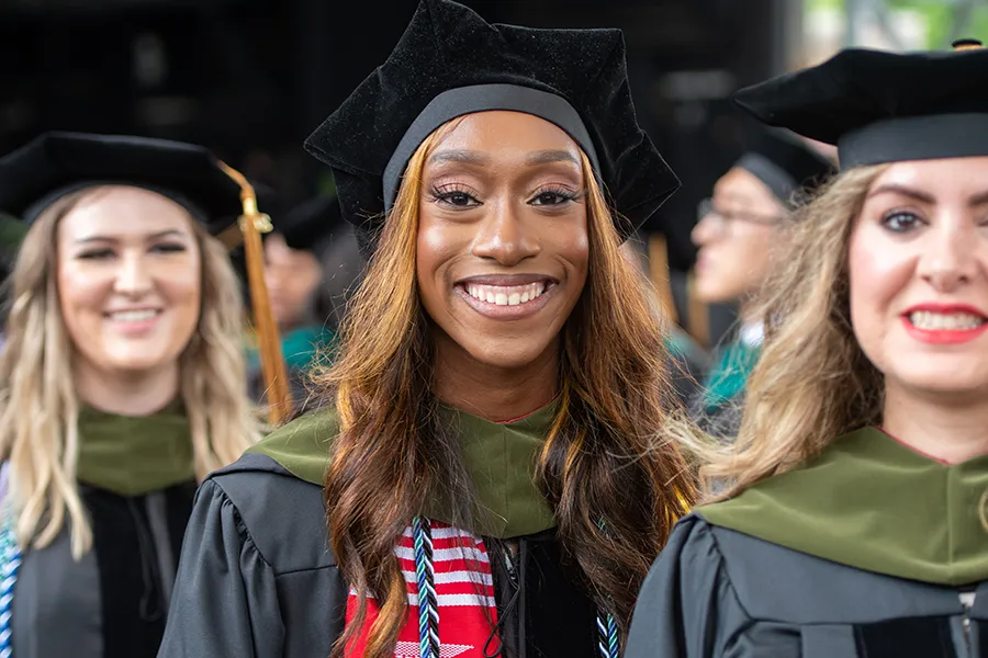 PCOM Georgia students smile in their caps, gowns and graduate garb during a commencement ceremony.