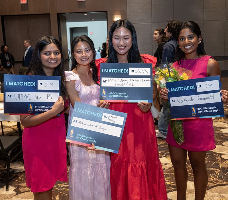 Group of students wearing pink dresses show off their Match Day signs