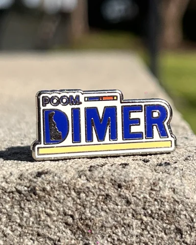 PCOM DIMER program acrylic pin sitting on paver block outside