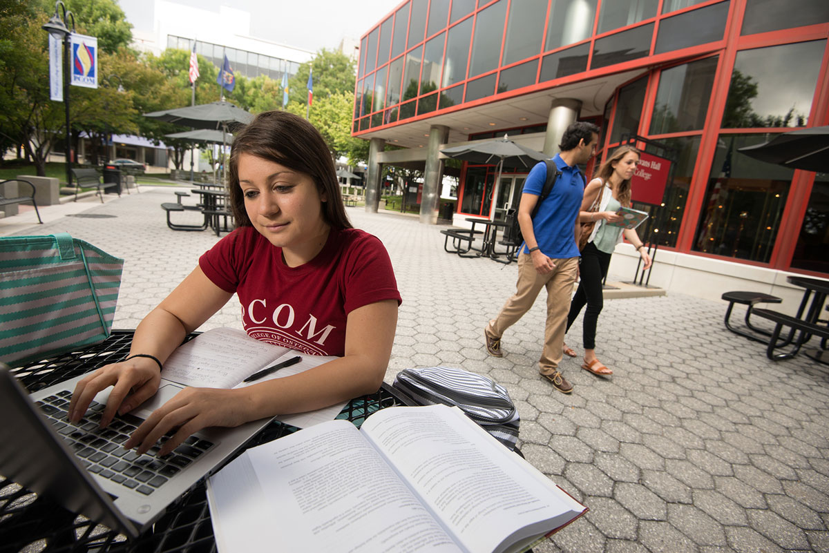 Female PCOM student sits outside and studies with her books and laptop.