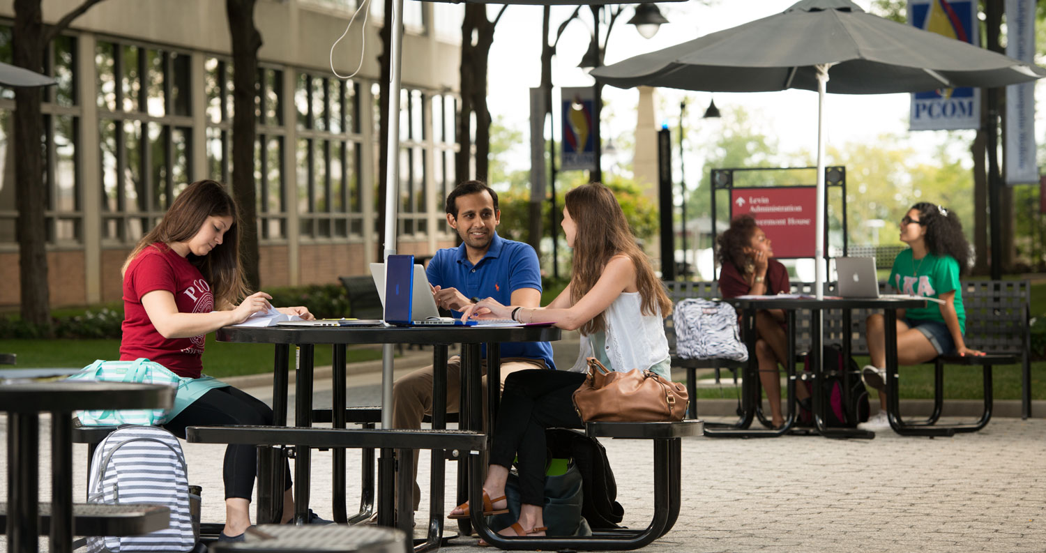 PCOM students smile and talk outside around round picnic tables