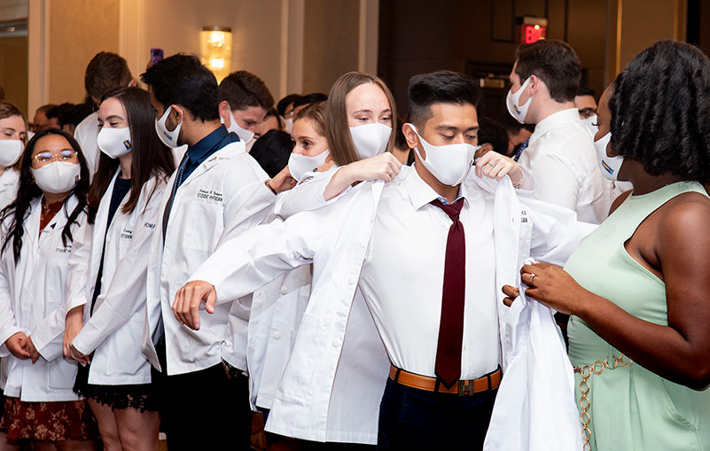 PCOM DO students help each other put on their physician white coats during the White Coat Ceremony