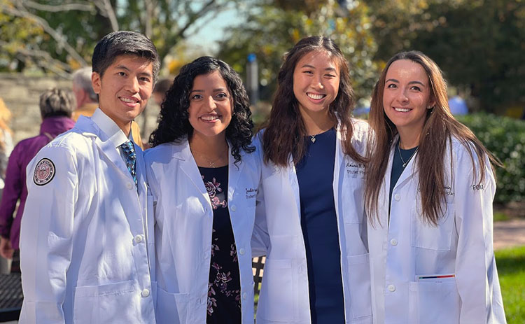 DO students smile outside of PCOM's Philadelphia campus donning their white coats