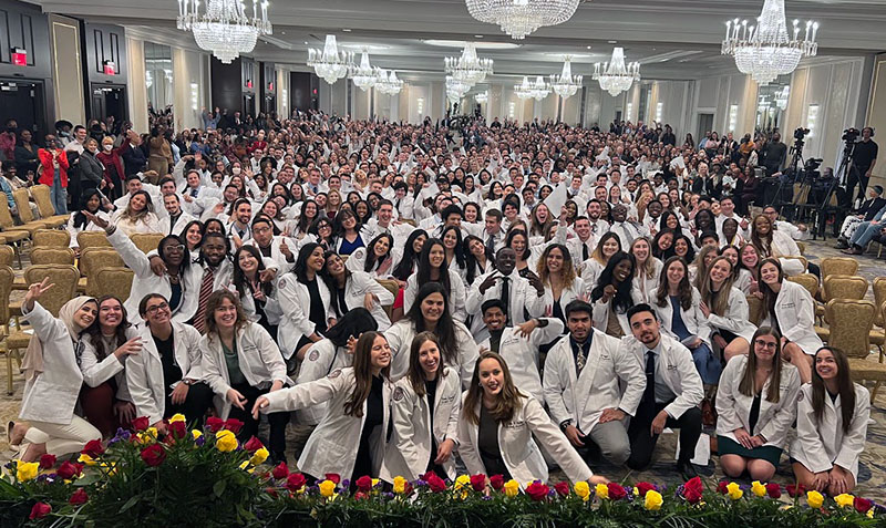 PCOM DO Class of 2026 smile and pose in a large group photo in a ballroom at the Hilton on City Ave